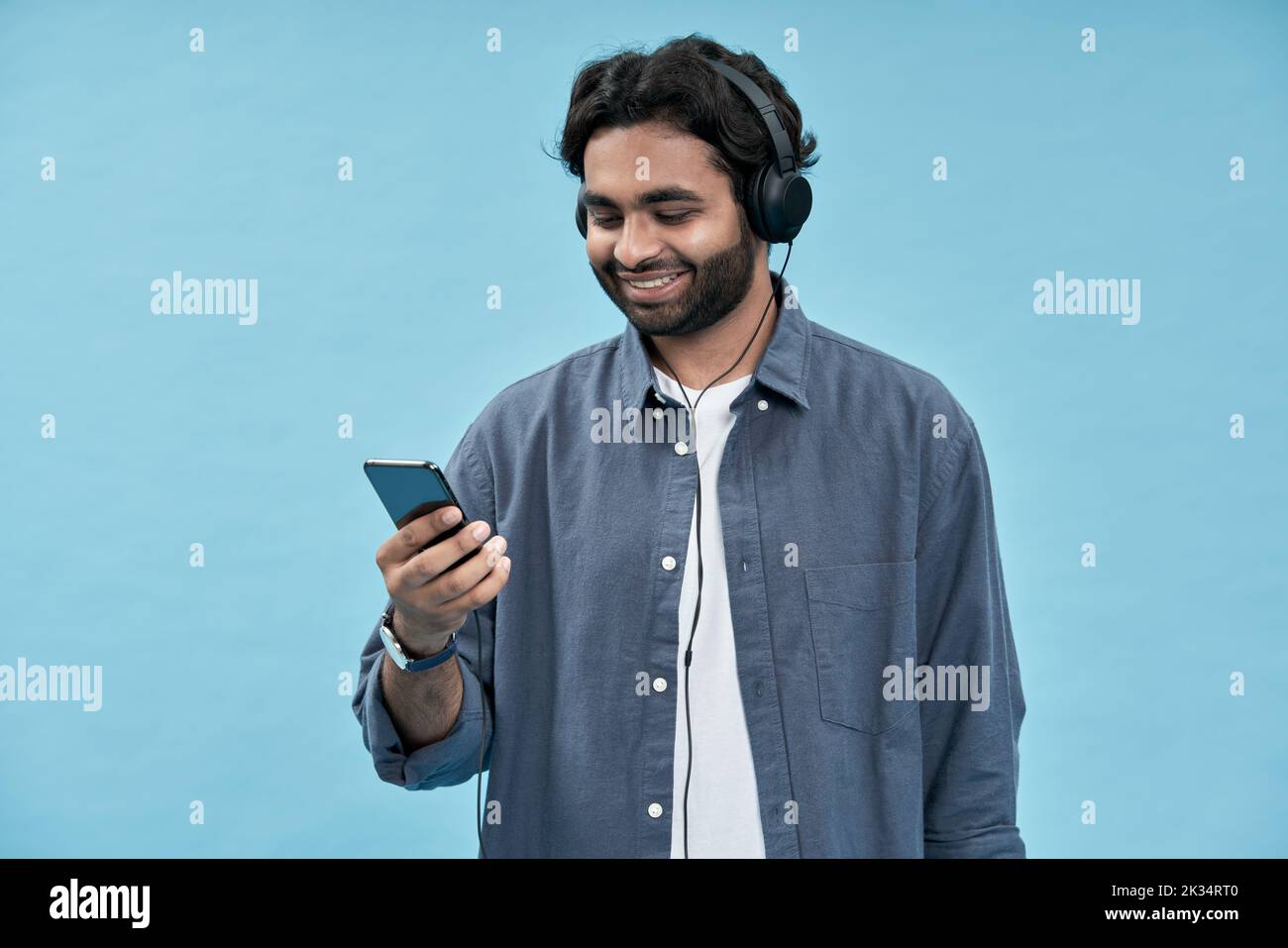 Young arab man wearing headphones using mobile phone isolated on blue. Stock Photo