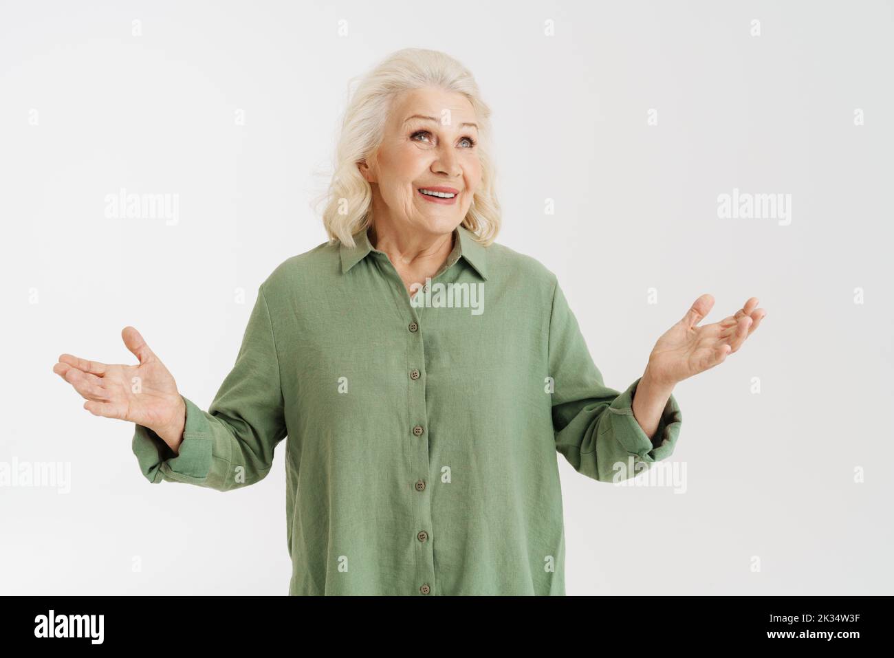 Grey senior woman in shirt smiling while gesturing at camera isolated over white background Stock Photo