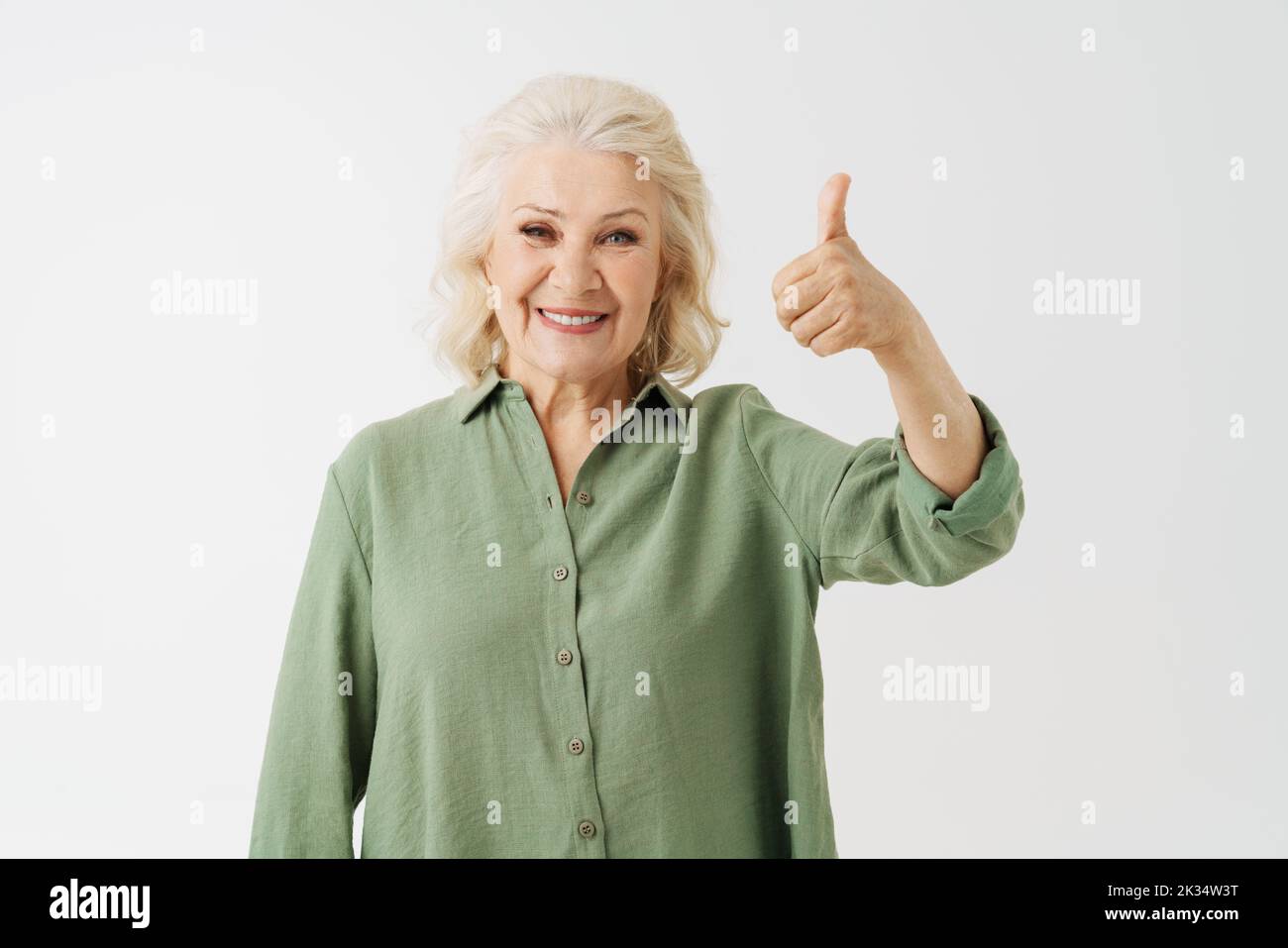 Grey senior woman in shirt smiling and gesturing thumb up isolated over white background Stock Photo