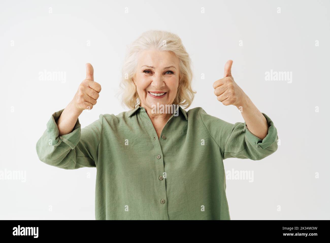 Grey senior woman in shirt smiling and gesturing thumbs up isolated over white background Stock Photo