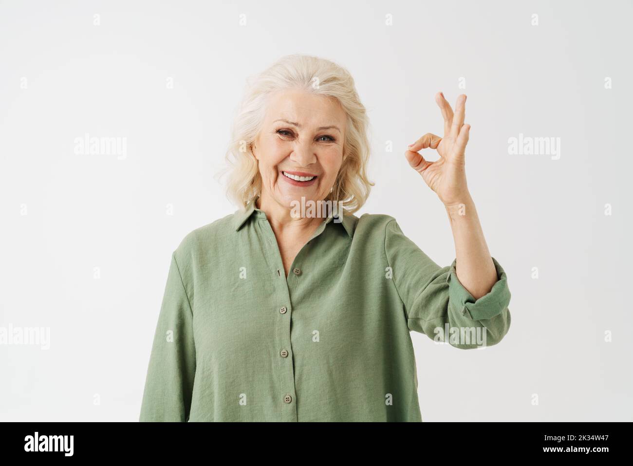 Grey senior woman in shirt smiling and gesturing ok sing isolated over white background Stock Photo