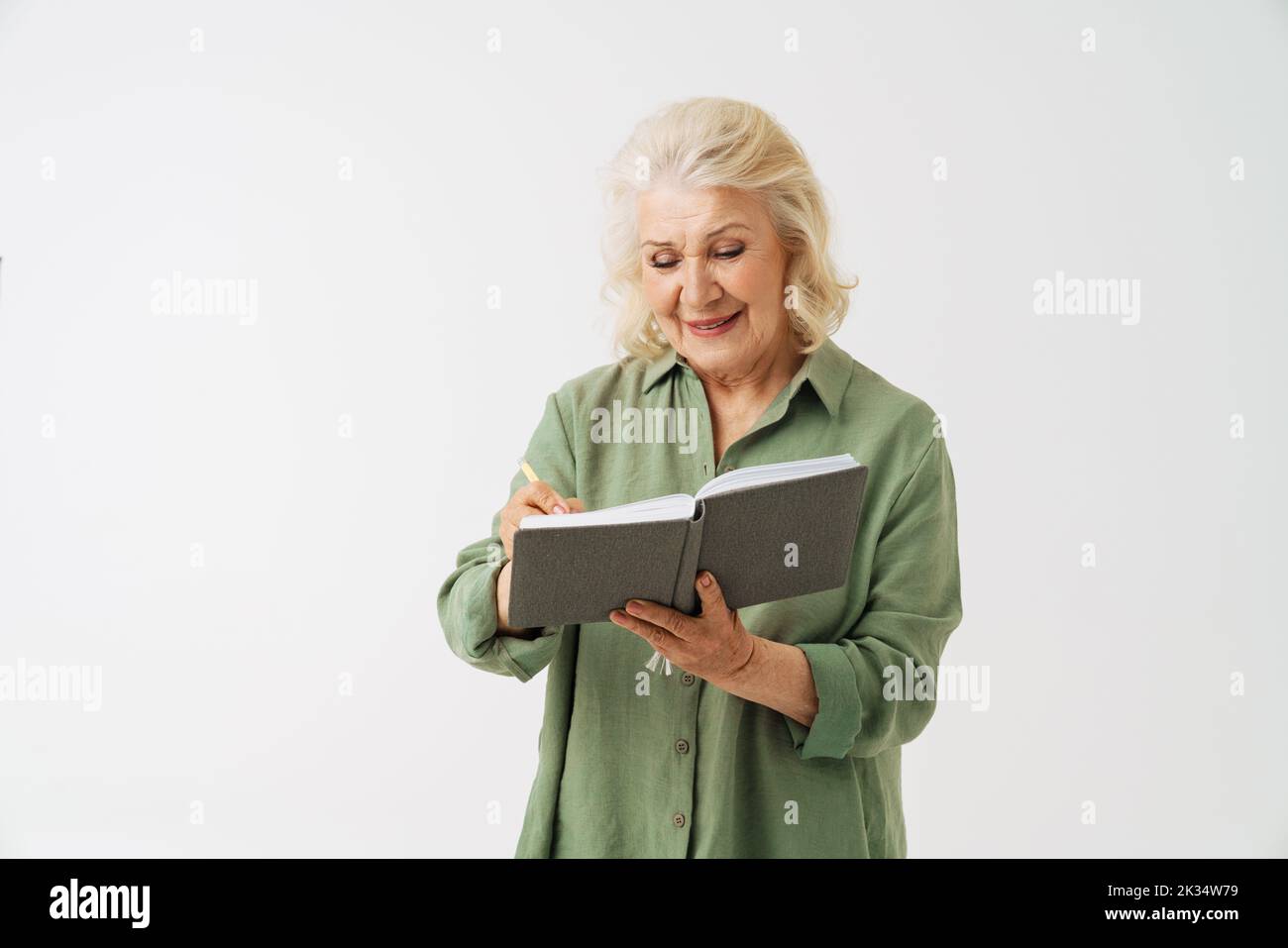 Grey senior woman smiling while writing down notes in planner isolated over white background Stock Photo