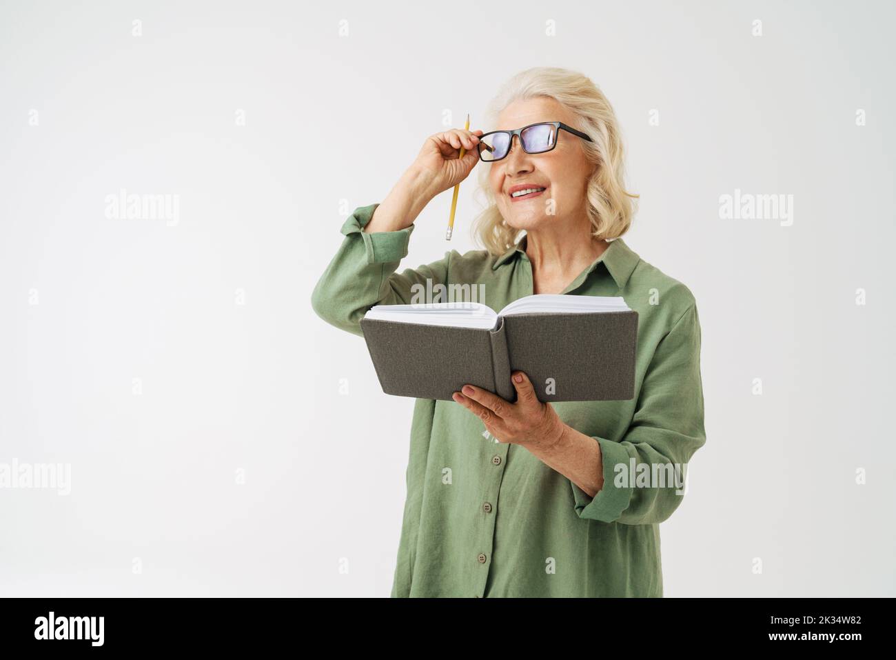 Grey senior woman in eyeglasses smiling while posing with planner isolated over white background Stock Photo