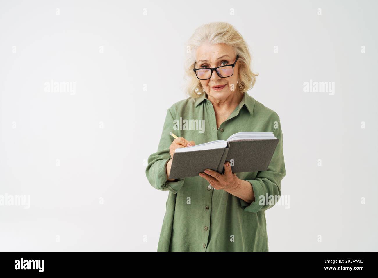 Grey senior woman in eyeglasses writing down notes in planner isolated over white background Stock Photo