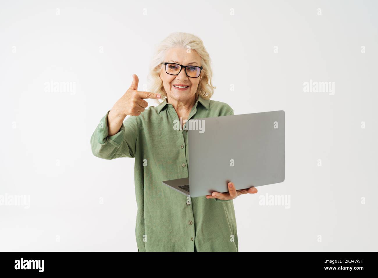 Grey senior woman in eyeglasses pointing finger at her laptop isolated over white background Stock Photo