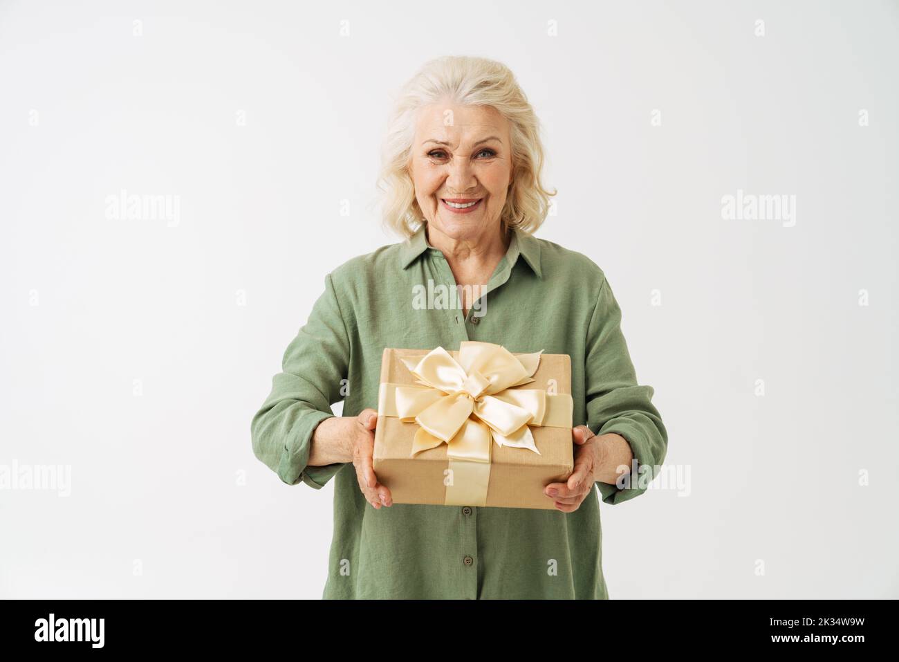 Grey senior woman smiling while showing gift box at camera isolated over white background Stock Photo