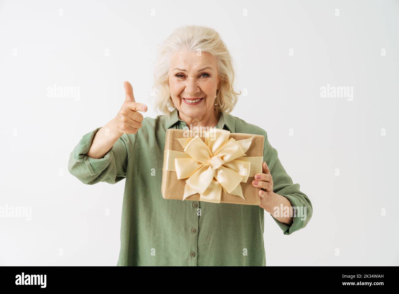 Grey senior woman pointing finger and showing gift box at camera isolated over white background Stock Photo