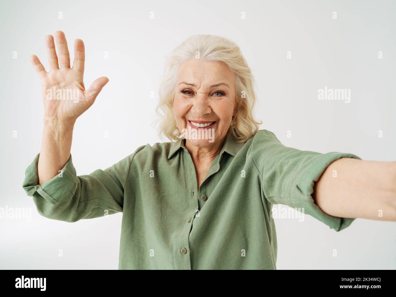 Grey senior woman smiling and gesturing while taking selfie photo isolated over white background Stock Photo