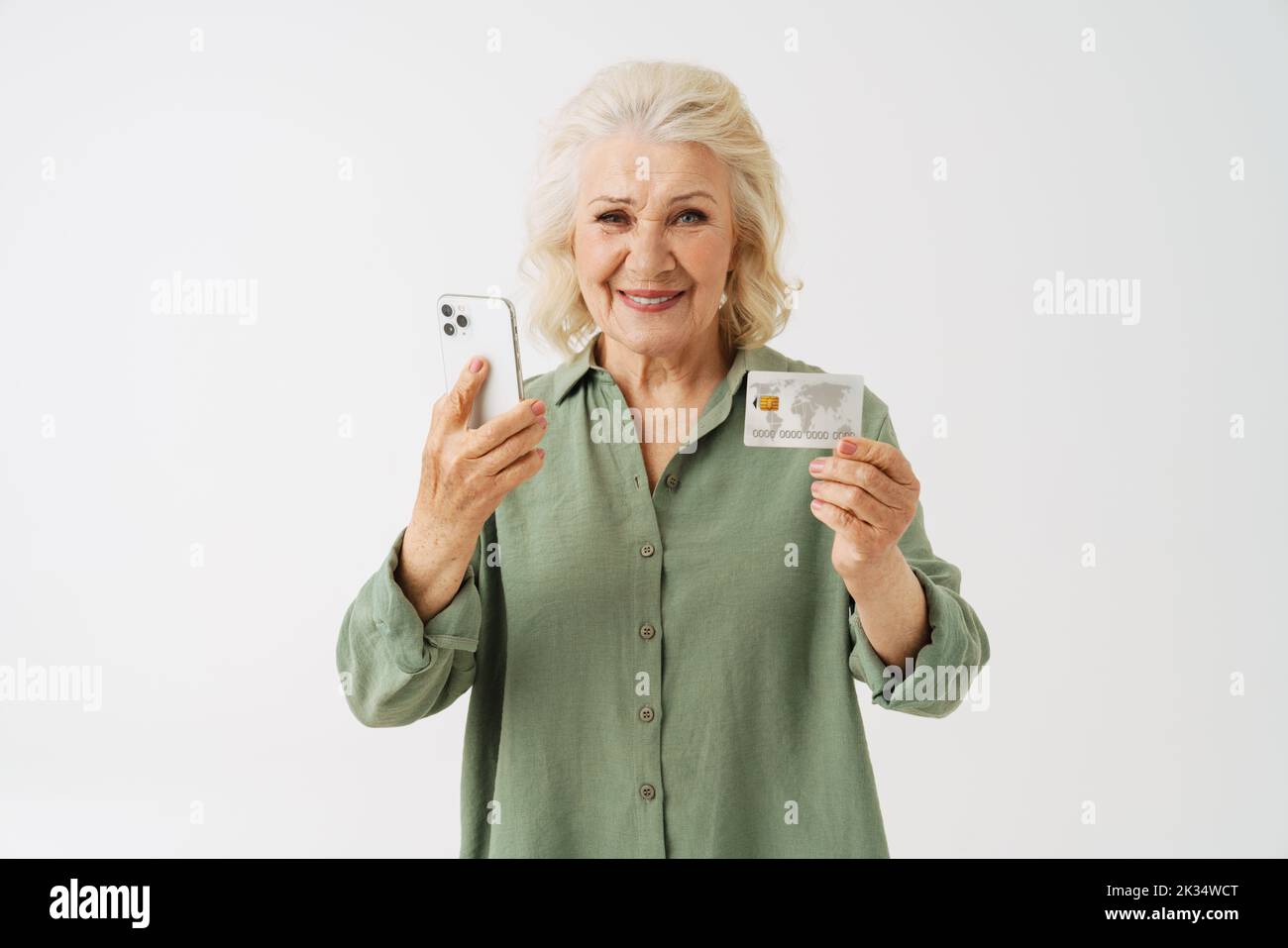 Grey senior woman smiling while showing cellphone and credit card isolated over white background Stock Photo