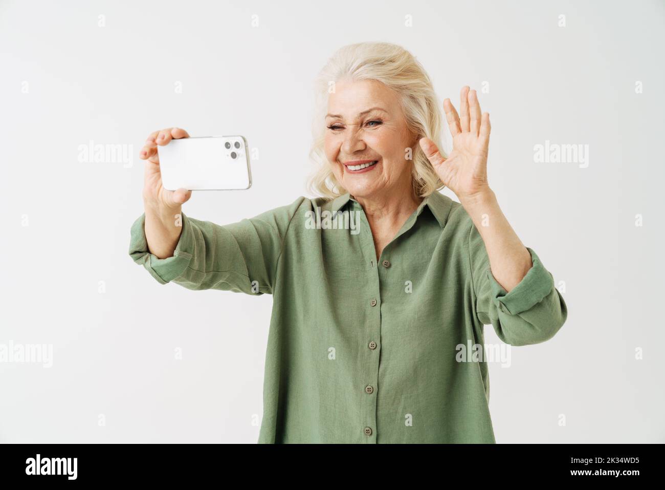 Grey senior woman gesturing while taking selfie on mobile phone isolated over white background Stock Photo