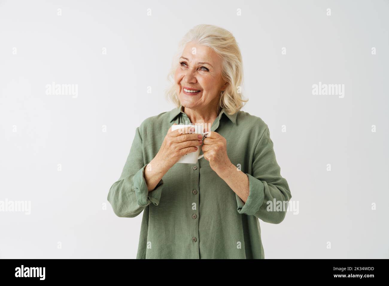 Grey senior woman in shirt smiling and drinking coffee isolated over white background Stock Photo