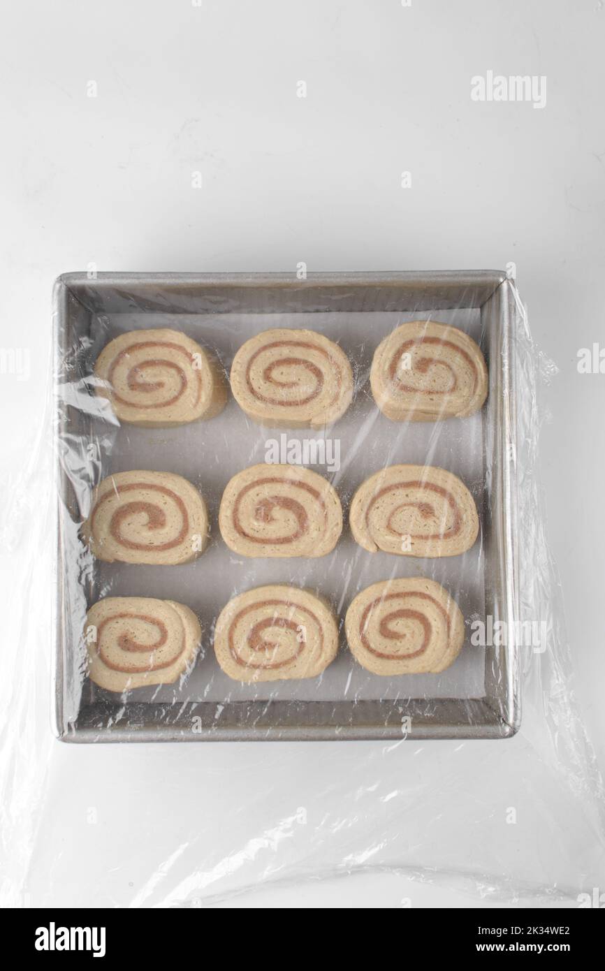 Cinnamon roll dough in pan covered with cling film, raw morning buns or