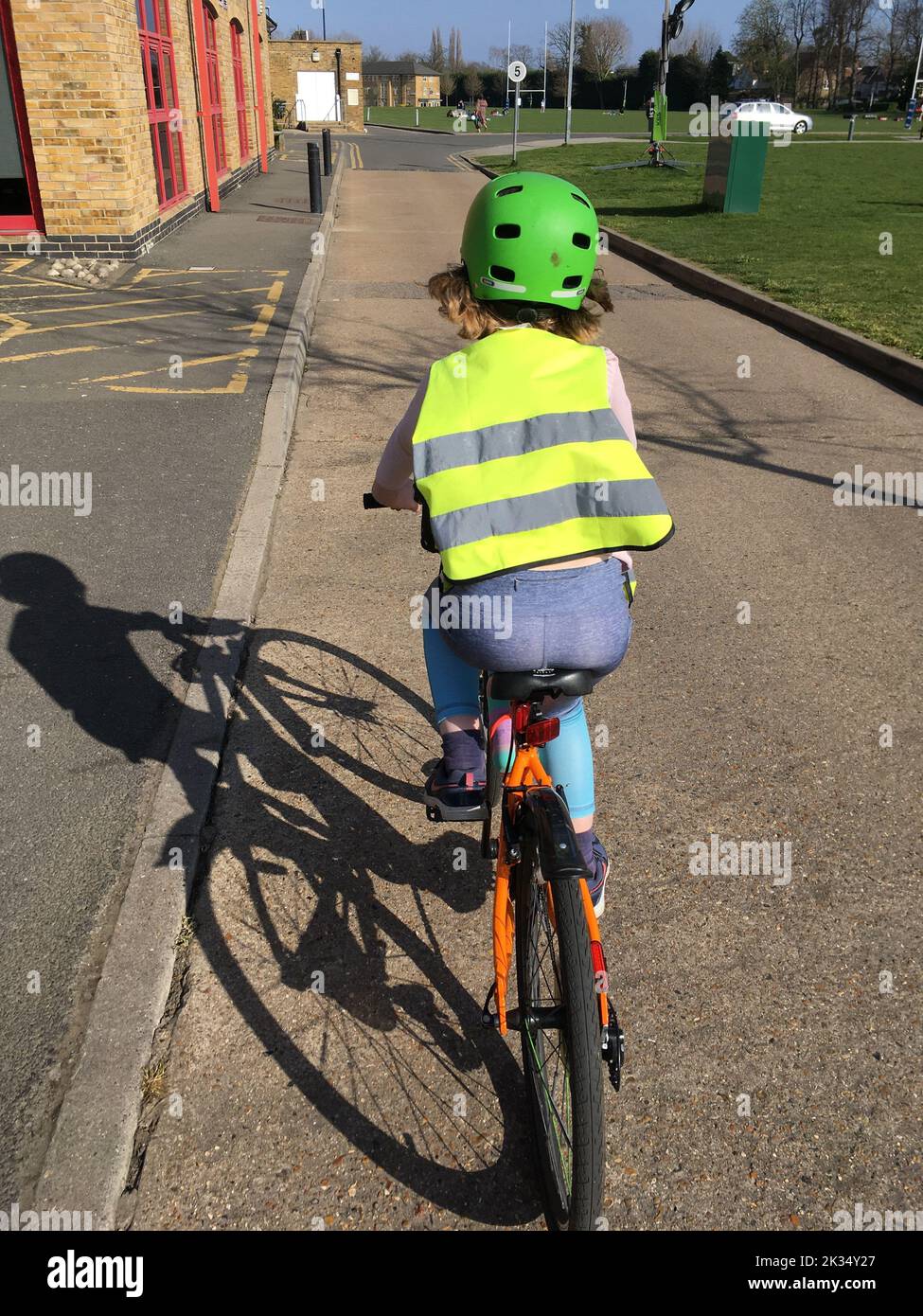 A seven year old girl cyclist rider pedals her bicycle / cycles safely wearing high visibility / hi vis clothing and a cycle helmet while she rides her bike on a sunny day. UK (132) Stock Photo
