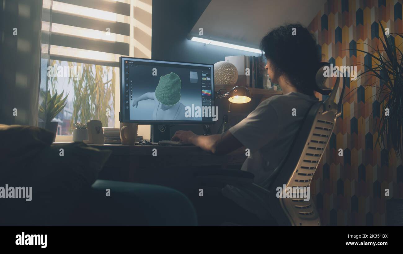 Guy sitting at the table and designing clothes in 3D modeling professional program on personal computer while working remotely from home Stock Photo