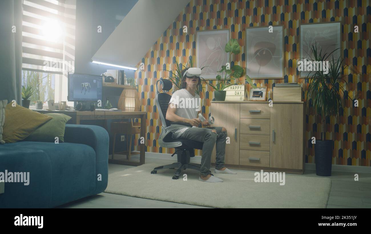 Man playing video game using modern VR headset and wireless controllers in leisure time in his room. Virtual reality device. Cyberspace and metaverse Stock Photo
