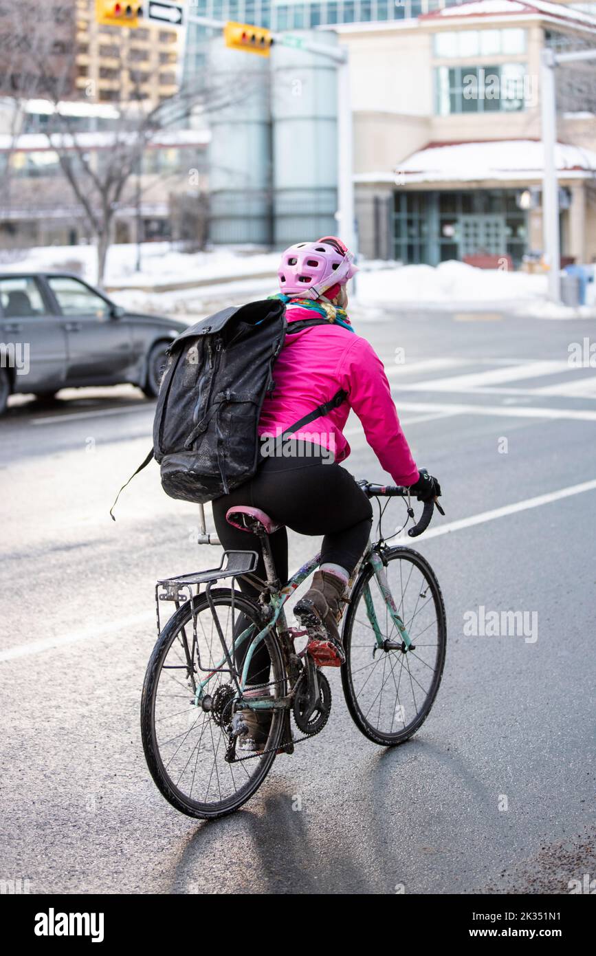 Female bike messenger with bag riding bike on wet winter city street