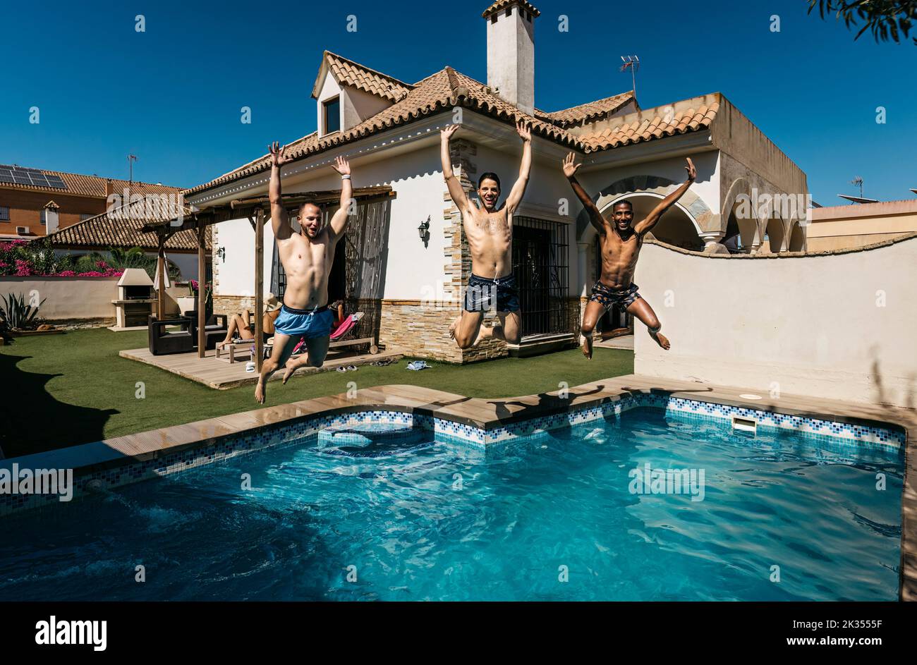 3 friends jumping into a pool in summer Stock Photo