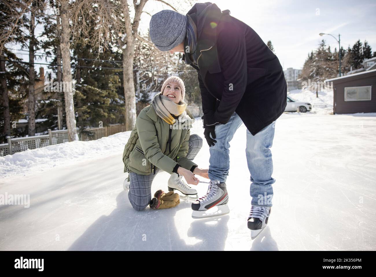 Happy girlfriend helping partner tie ice skate shoelace at winter park Stock Photo
