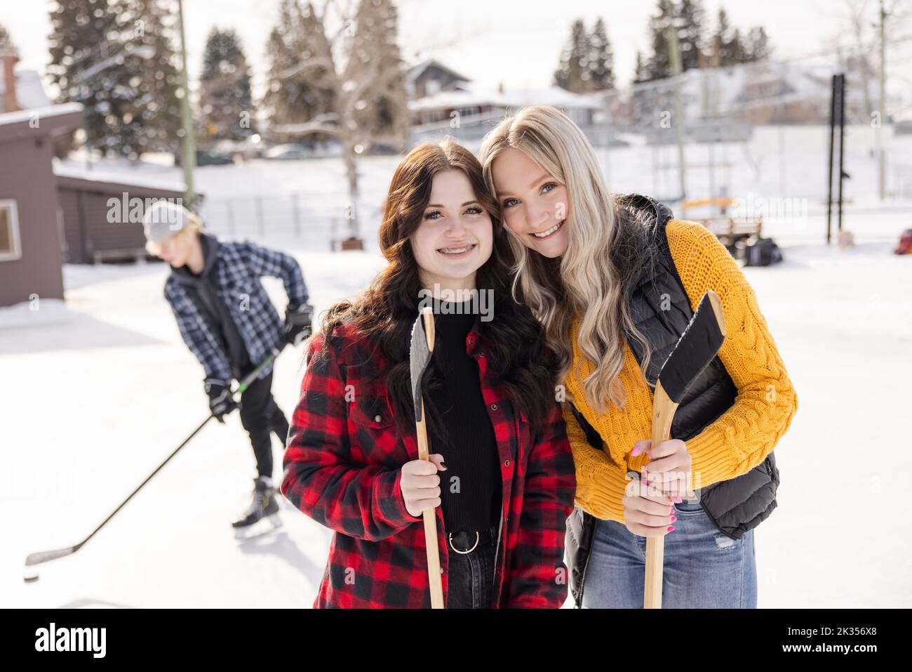 Portrait happy teenage girl friends playing ice hockey at ice rink Stock Photo