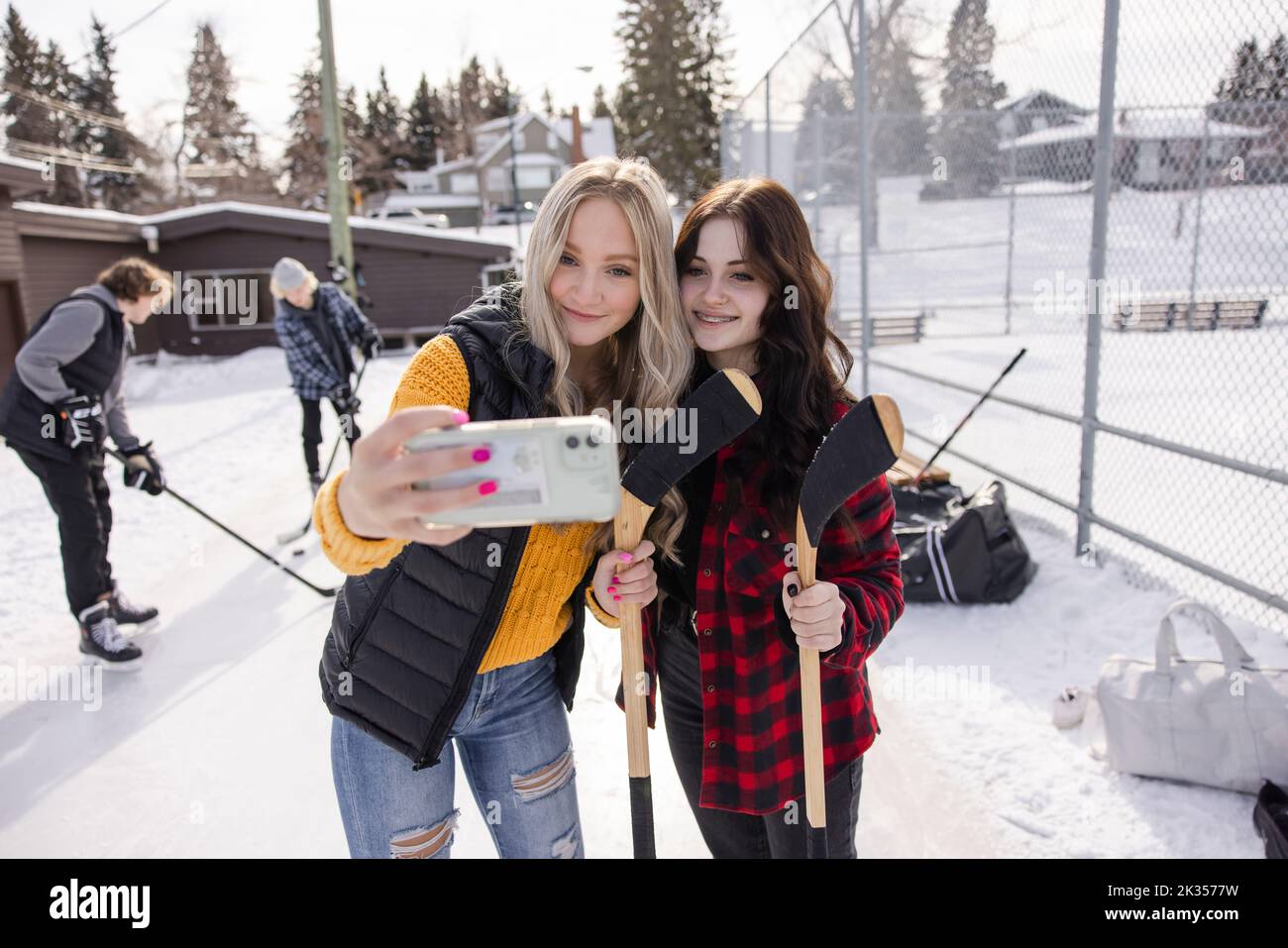 Happy teenage girl friends playing ice hockey taking selfie at park Stock Photo