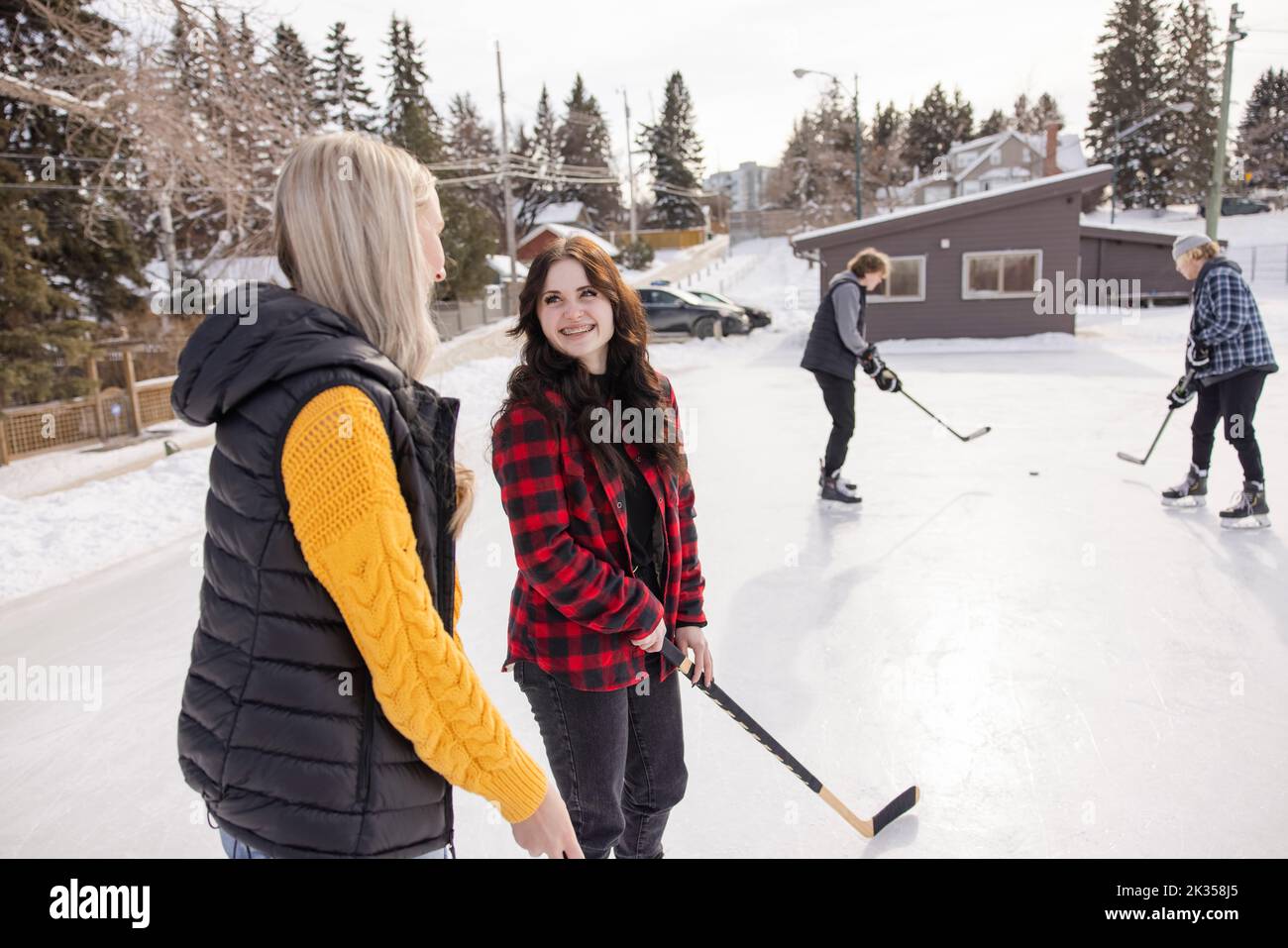 Happy teenage girl friends playing ice hockey at winter ice rink Stock Photo