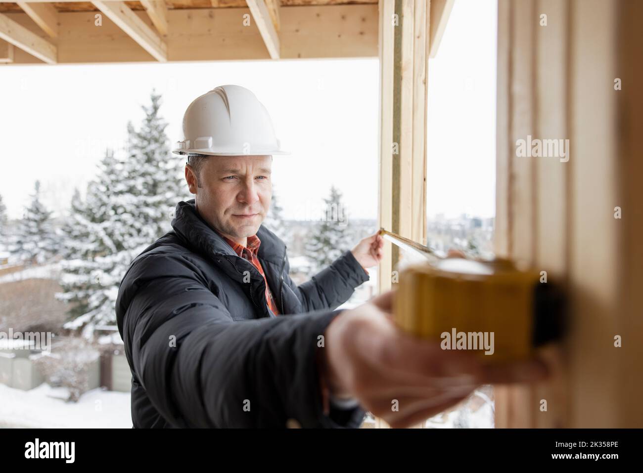 Male homebuilder measuring framing at winter construction site Stock