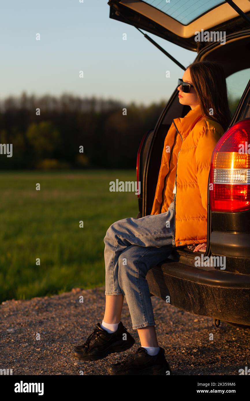 Pretty sad teenage girl with sun glasses sitting alone in a car trunk ...