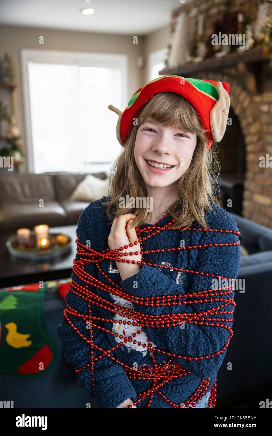 Portrait happy preteen girl wrapped in red beaded Christmas garland Stock Photo