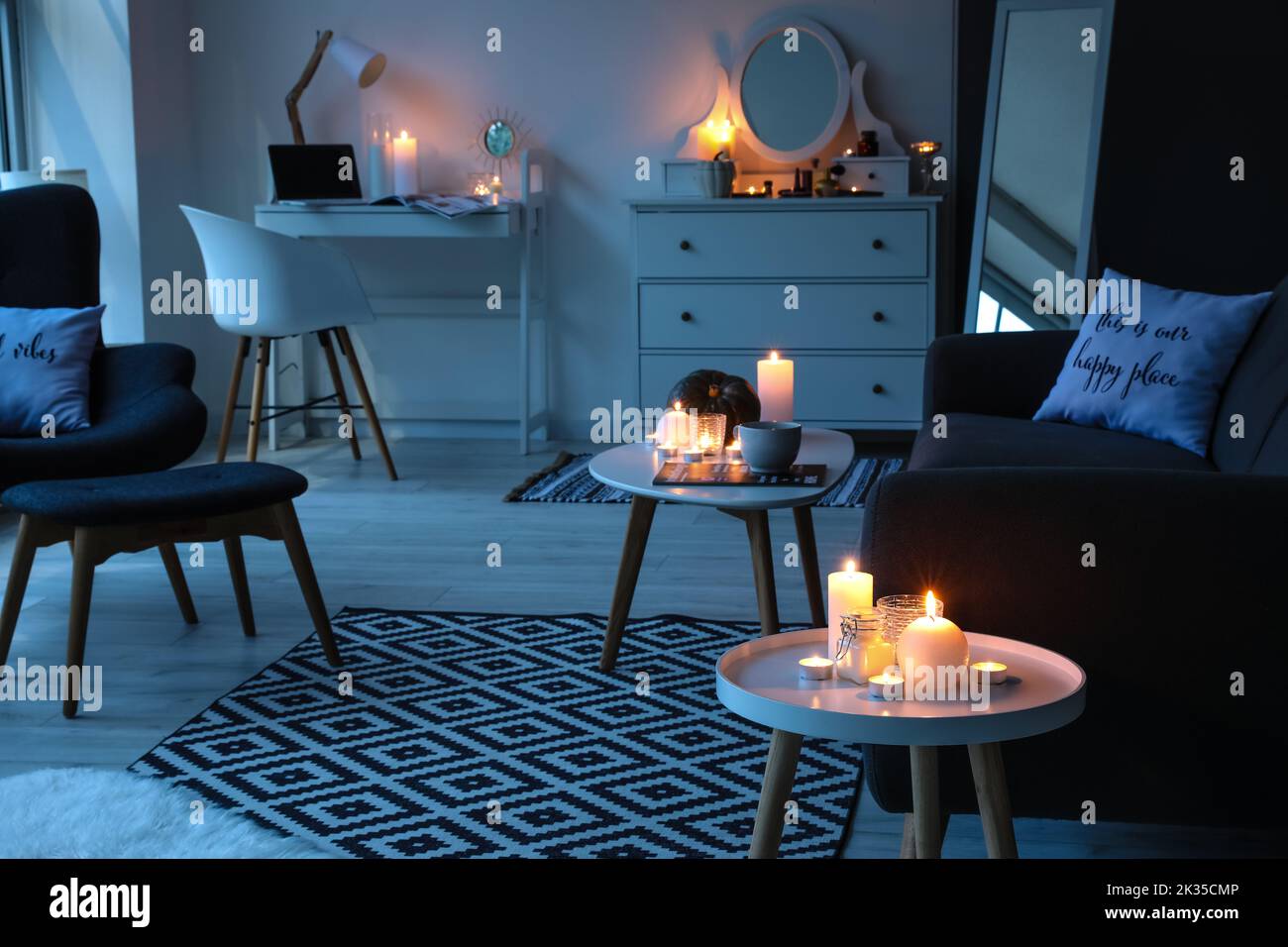 Interior of living room with burning candles, workplace and armchair