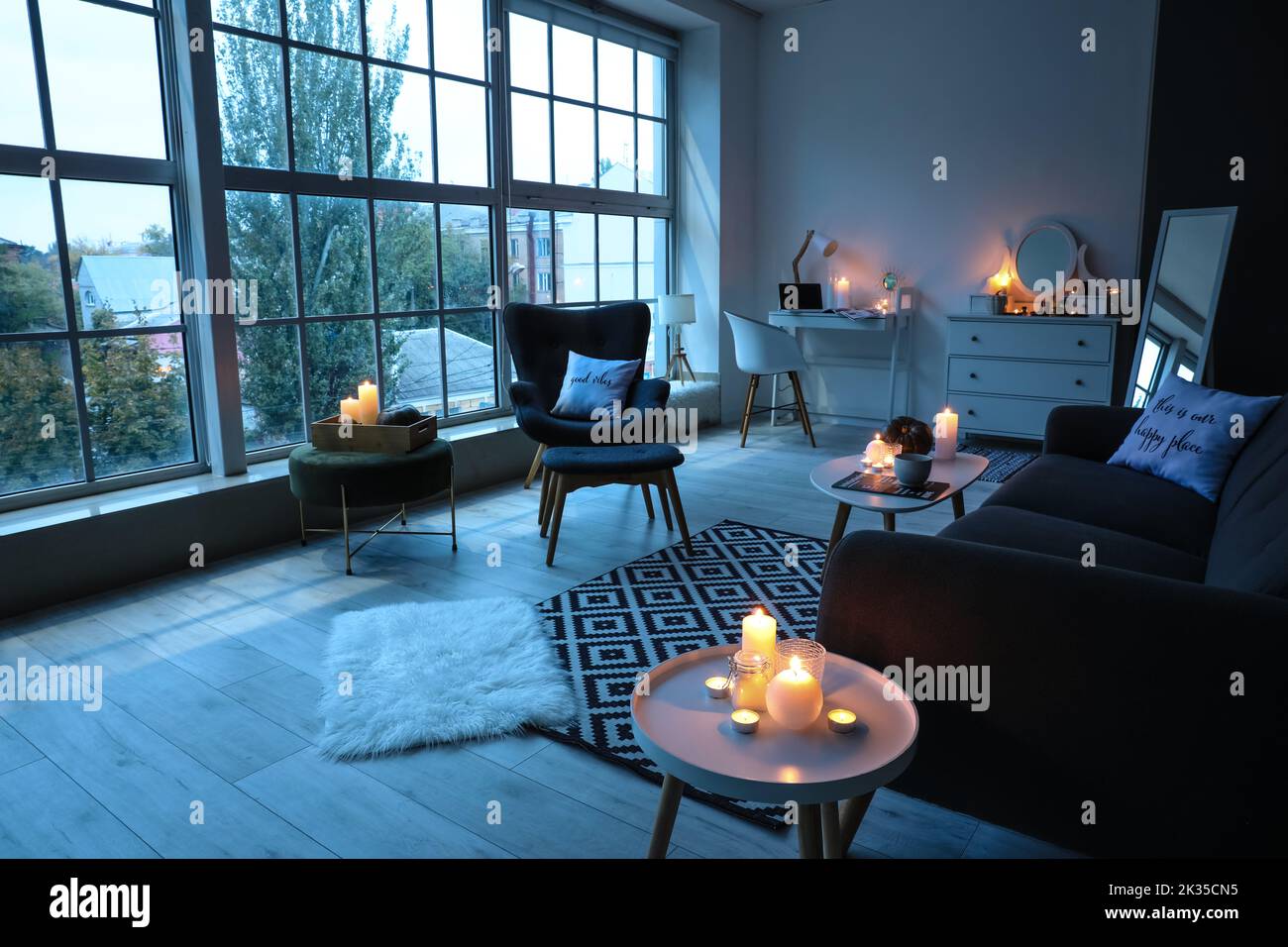 Interior of living room with burning candles, workplace and armchair