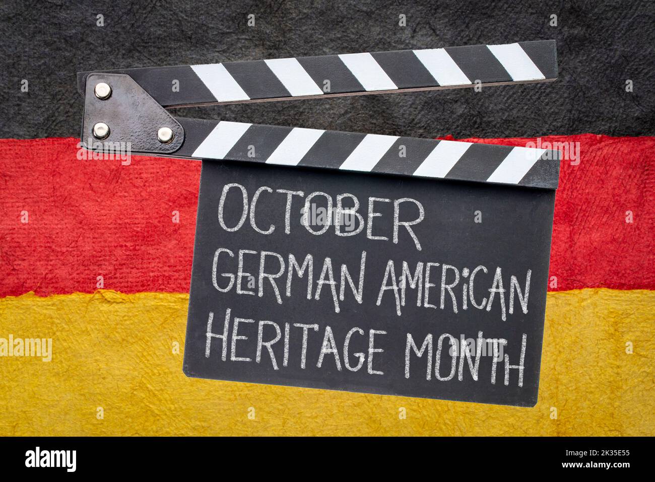 October - German American Heritage Month, white chalk text on a clipboard against paper abstract in colors of Germany national flag, reminder of cultu Stock Photo