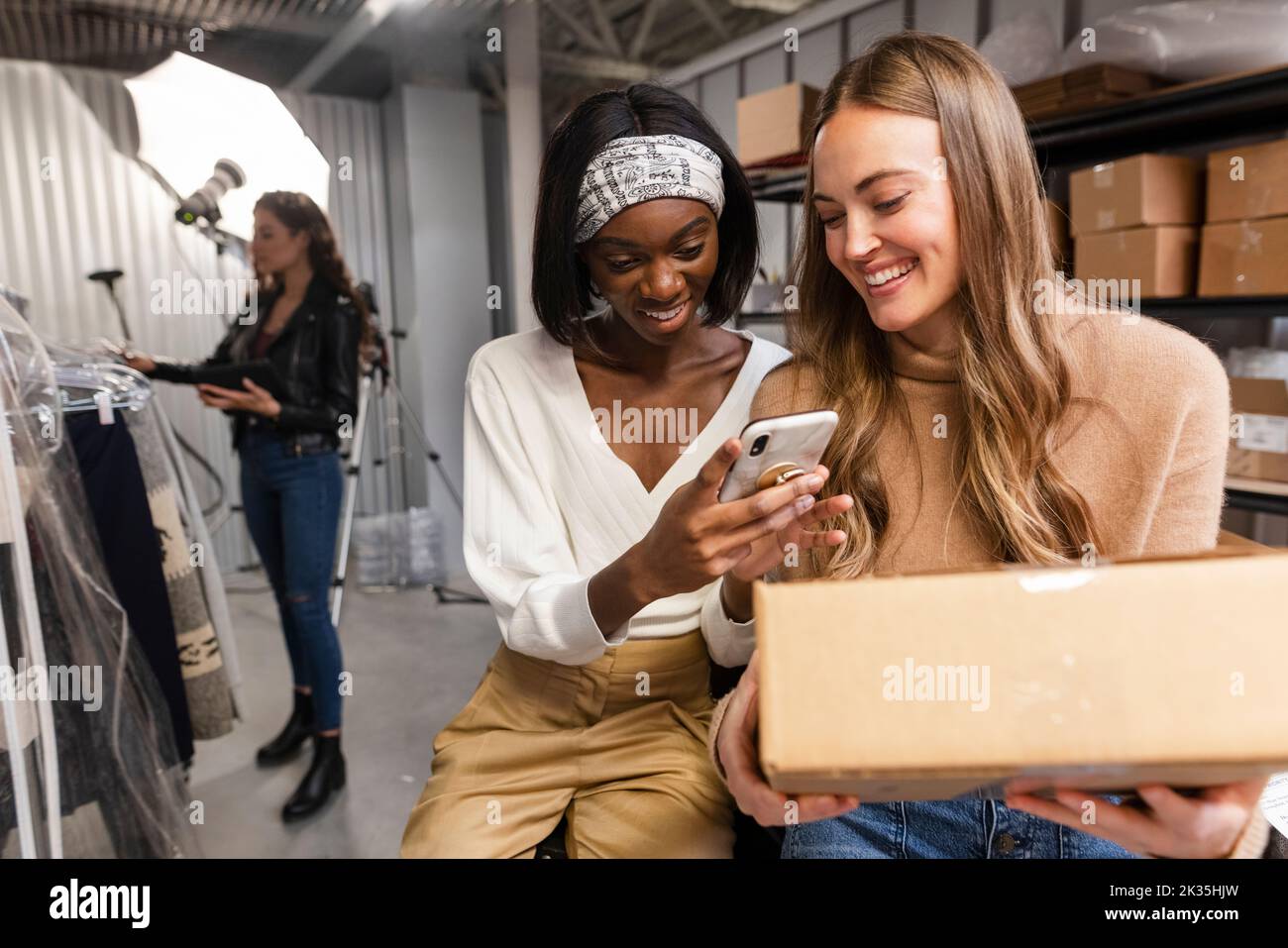 Female consignment workers with phone and box in storage facility Stock