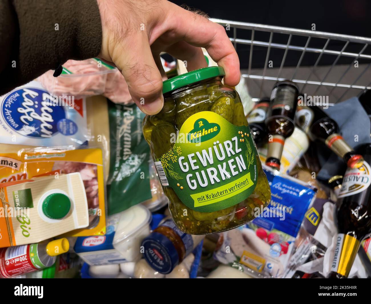 Frankfurt, Germany - Sep 17, 2022: POV male hand with a full shopping cart of groceries at a convenience store holding Kuhne Gewurz gurken - pickled gherkin Stock Photo