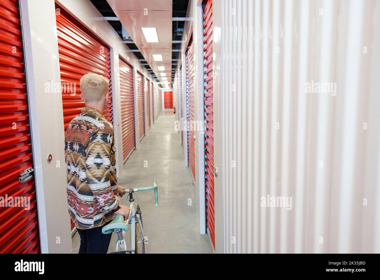 Young man moving bicycle in storage facility corridor Stock Photo