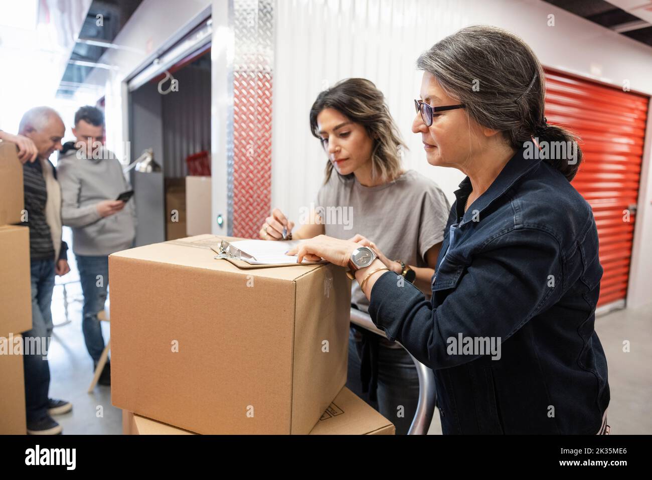 Senior mother and daughter with clipboard and box in storage facility