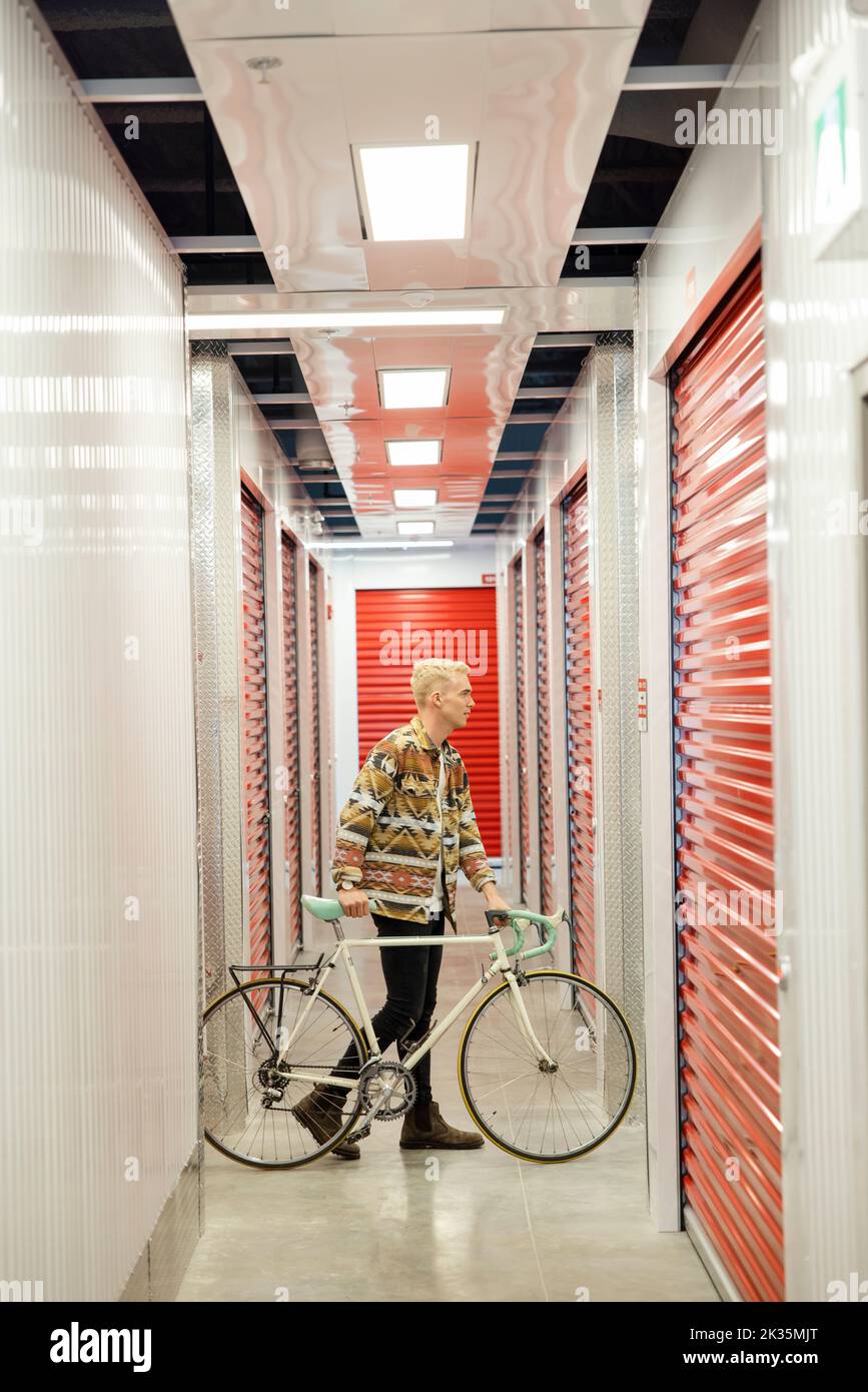 Young man with bicycle in storage facility corridor Stock Photo