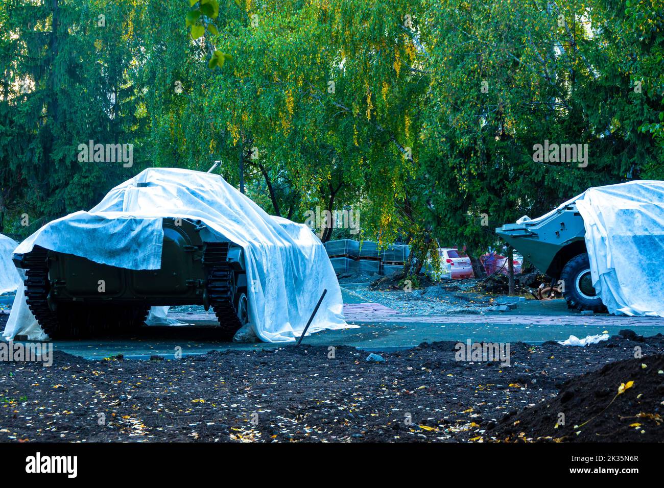 lightly armored military equipment covered with tarpaulin stands in the city park during repair work, selective focus Stock Photo