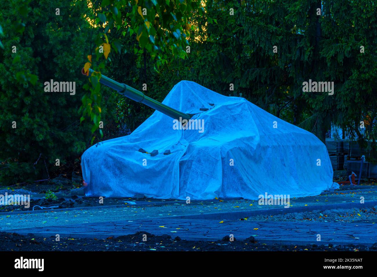 military tracked vehicles covered with a tarpaulin stand on the edge of a city park, selective focus Stock Photo