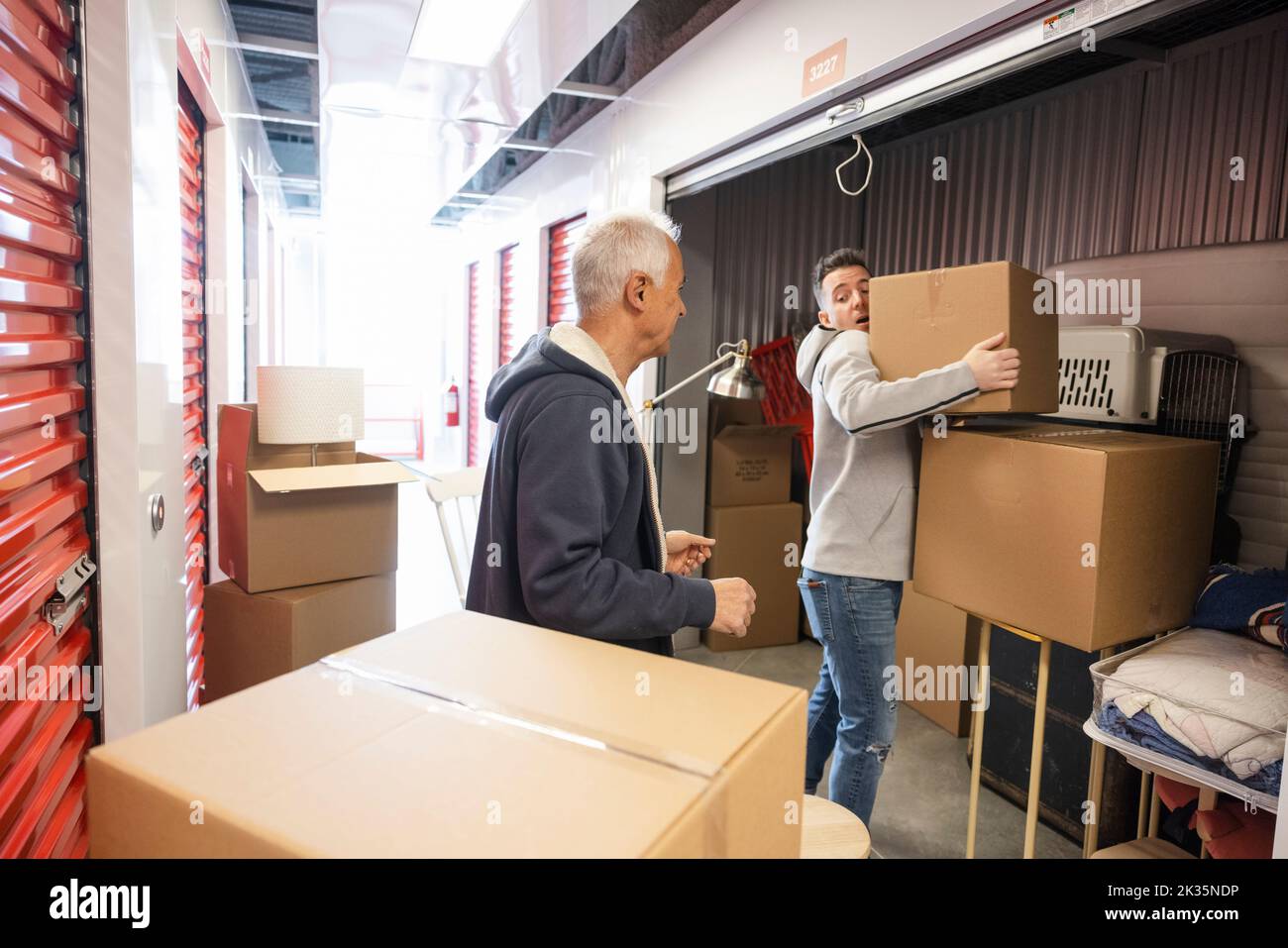 Son helping senior father move boxes out of storage facility locker Stock Photo