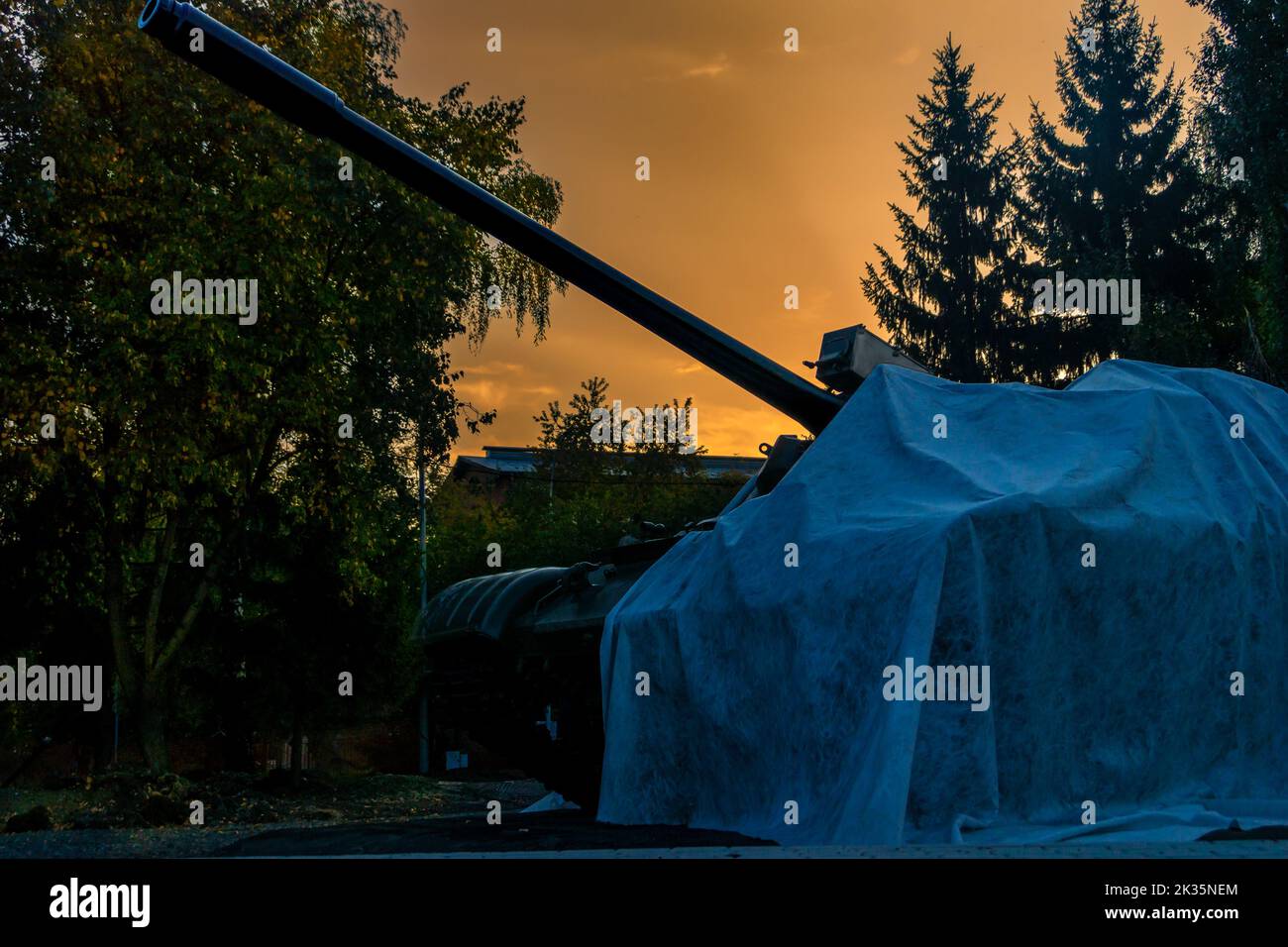 a tank covered with material stands in a city park against the background of an evening orange sky, selective focus Stock Photo