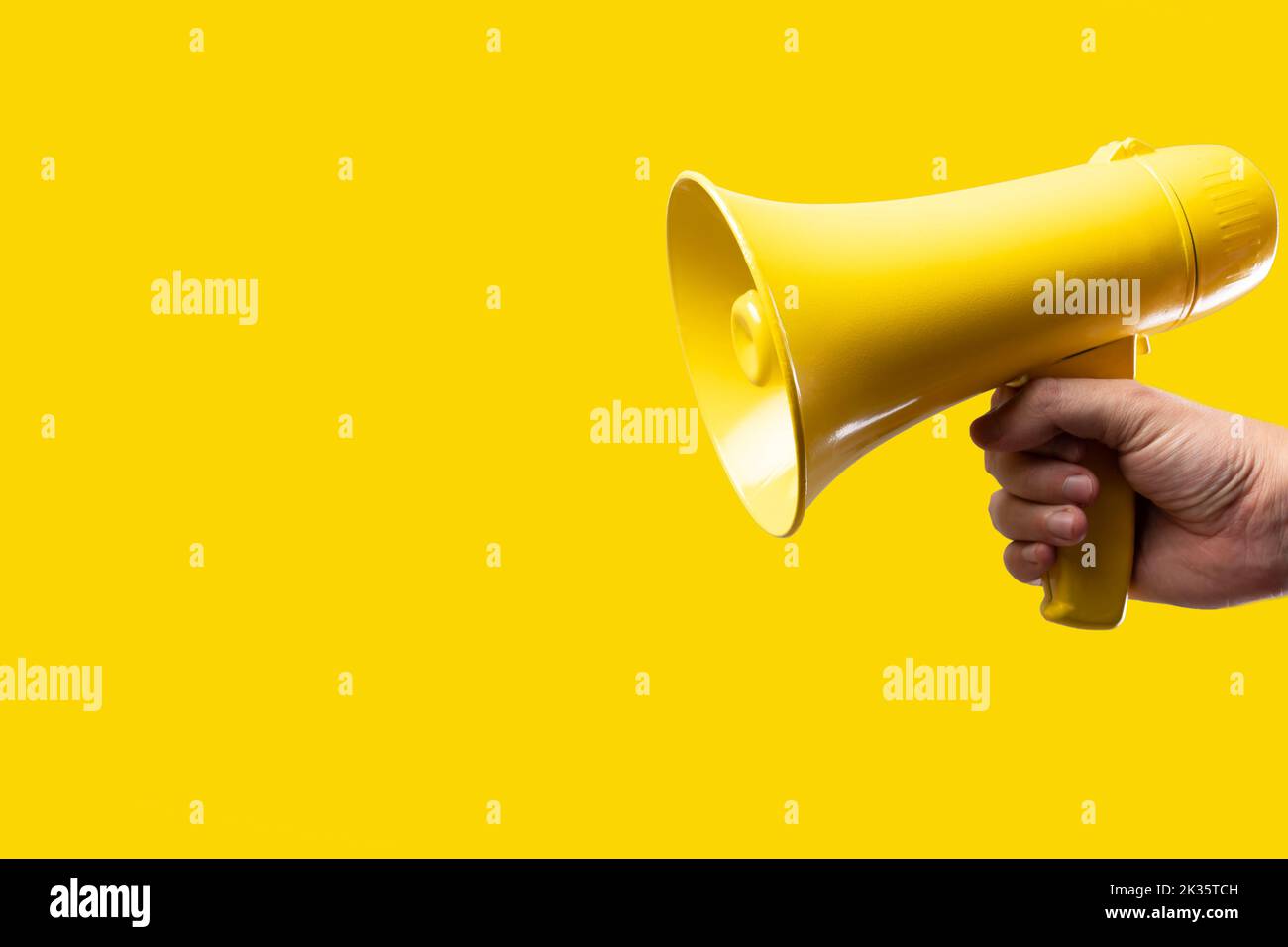 A man's hand holds a yellow megaphone on a bright yellow background. Rumors, fakes, agitation, propaganda, election debates, journalism, media, busine Stock Photo