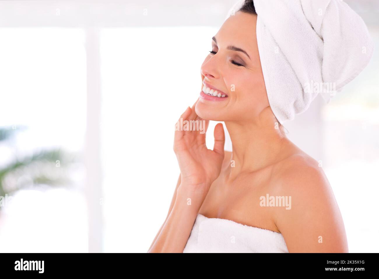 She gives her skin lots of TLC. A woman caressing her skin while standing with her towel wrapped