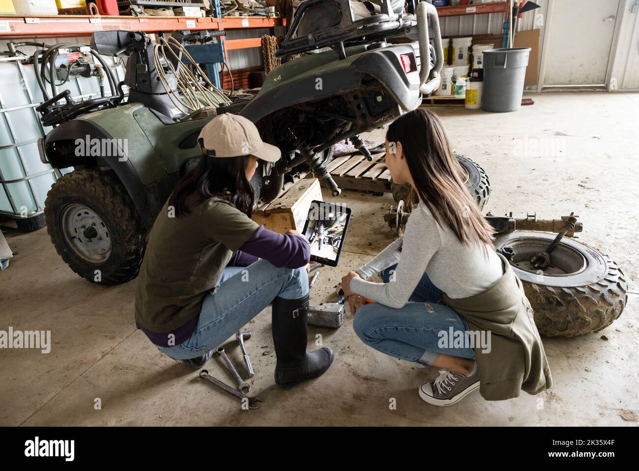 Mother and daughter farmers with digital tablet fixing quadbike Stock