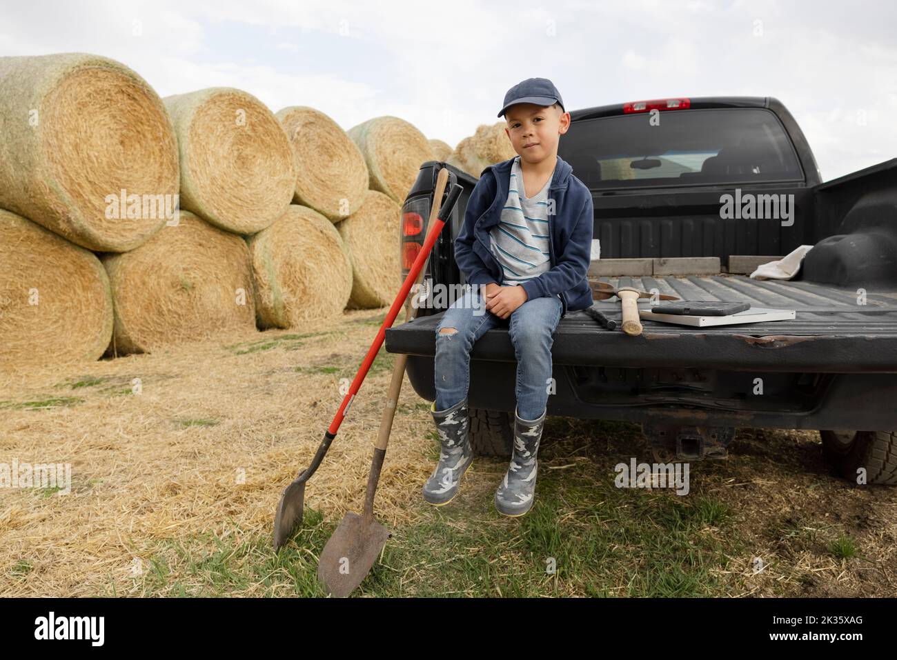 Portrait boy sitting on pickup truck tailgate on rural farm Stock Photo