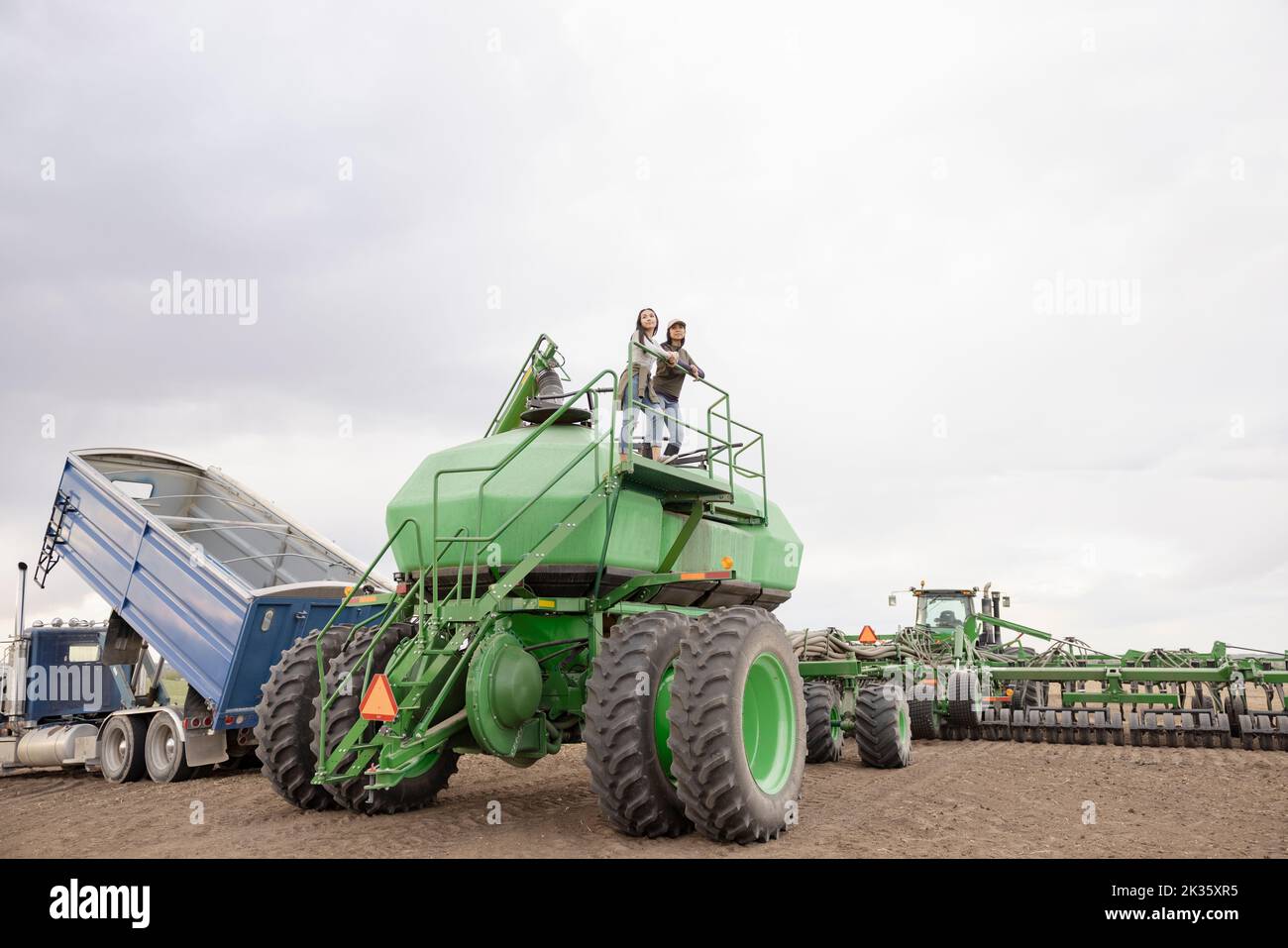Mother and daughter farmers on farming equipment platform on farm Stock
