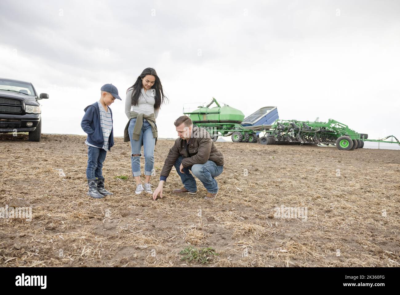 Farmer family inspecting crop soil on rural farm Stock Photo
