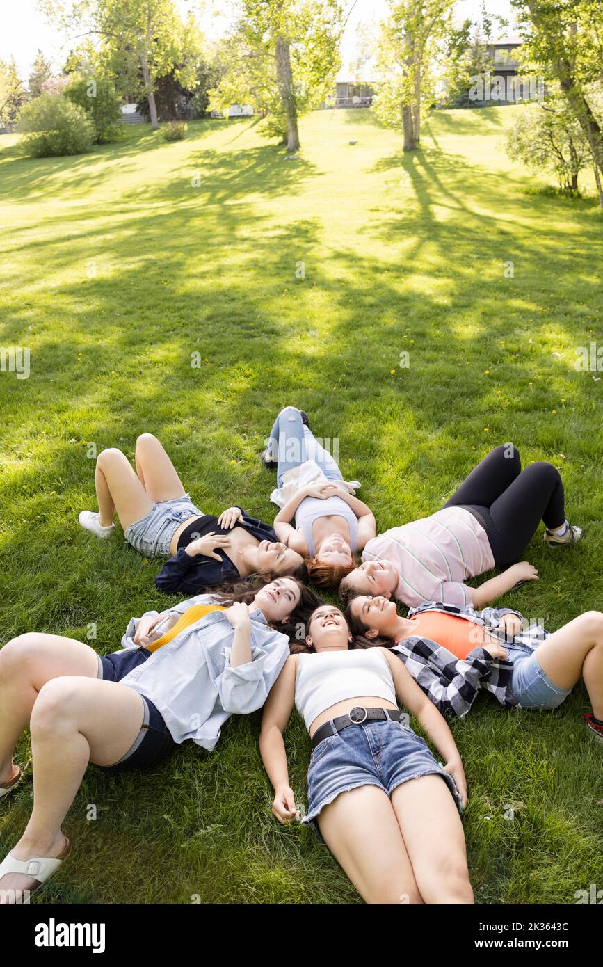 Classmates lying down on grass in park Stock Photo