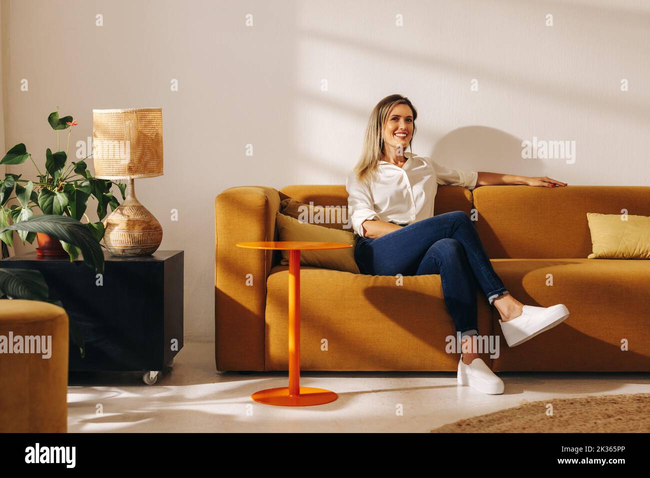 Happy businesswoman smiling at the camera while sitting on a couch in an office lobby. Cheerful young businesswoman working in a creative coworking of Stock Photo