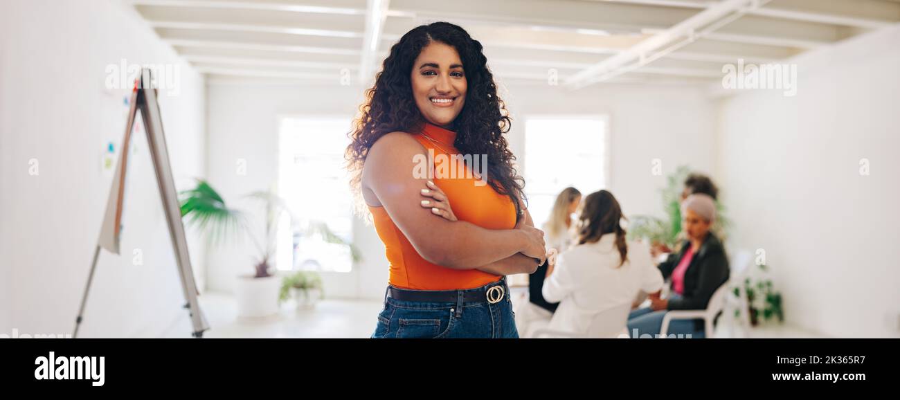 Happy young businesswoman smiling at the camera while standing in a creative office. Cheerful young businesswoman attending a meeting with her colleag Stock Photo