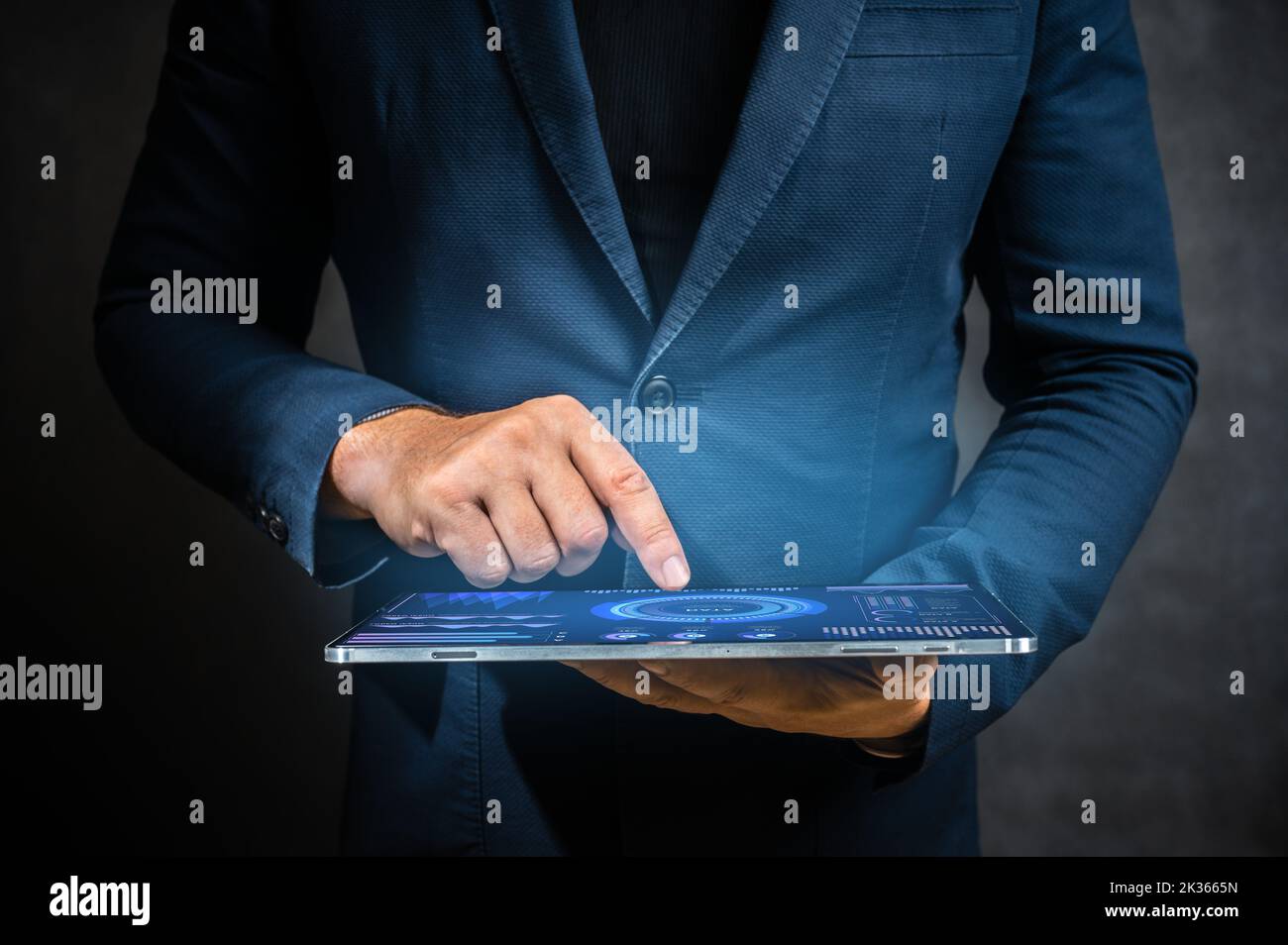 Businessman holding tablet computer on dark background. Businessman uses modern digital technology to manage business. man in suit holds digital table Stock Photo